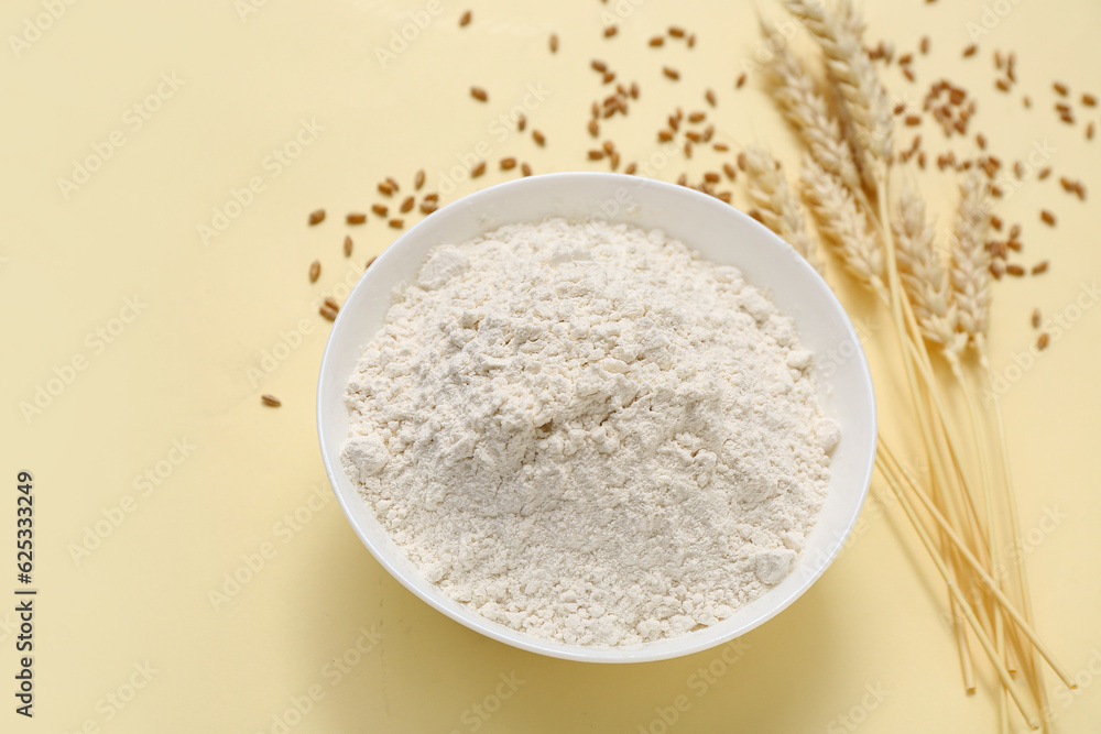 Bowl with wheat flour and spikelets on yellow background