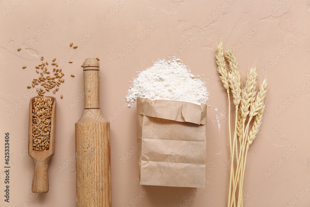 Paper bag with wheat flour, rolling pin, grains and spikelets on brown background