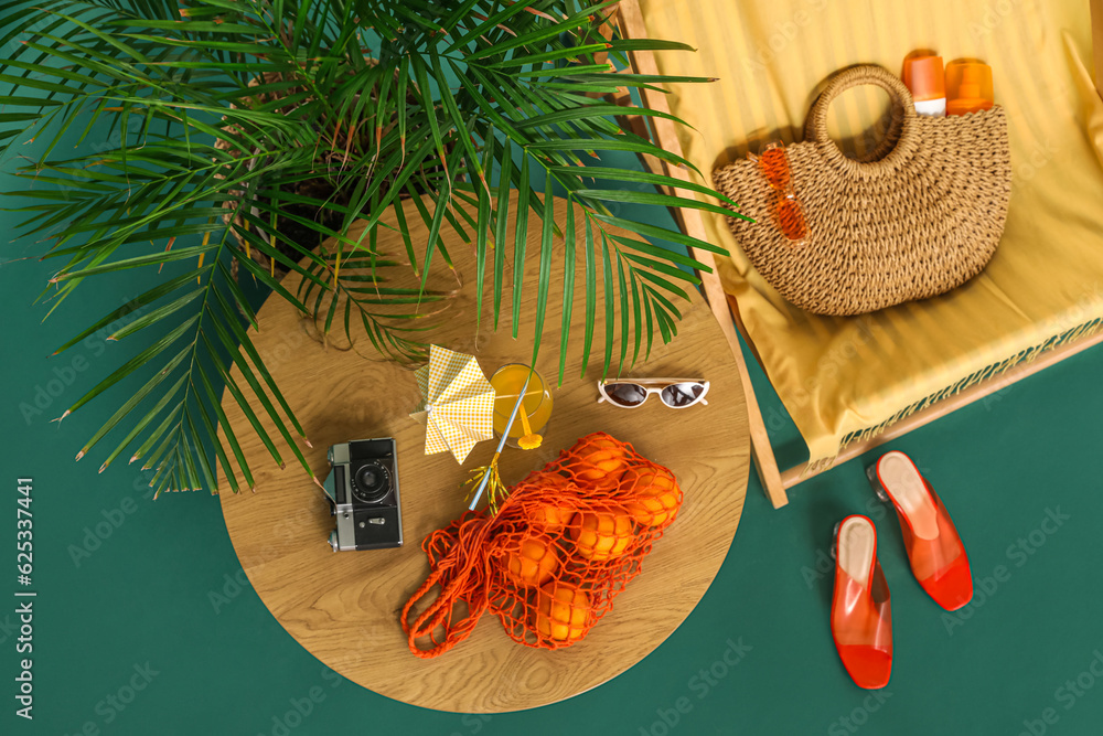 Deckchair, beach accessories, palm tree and oranges on color background