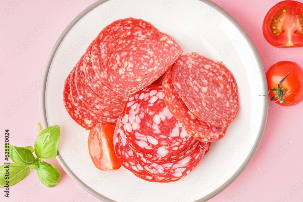 Plate with slices of tasty salami on pink background