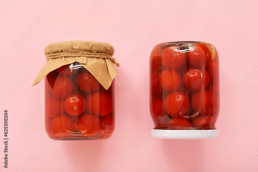 Jars with canned tomatoes on pink background