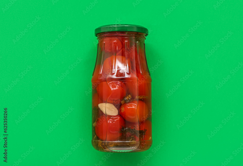 Jar with canned tomatoes on green background