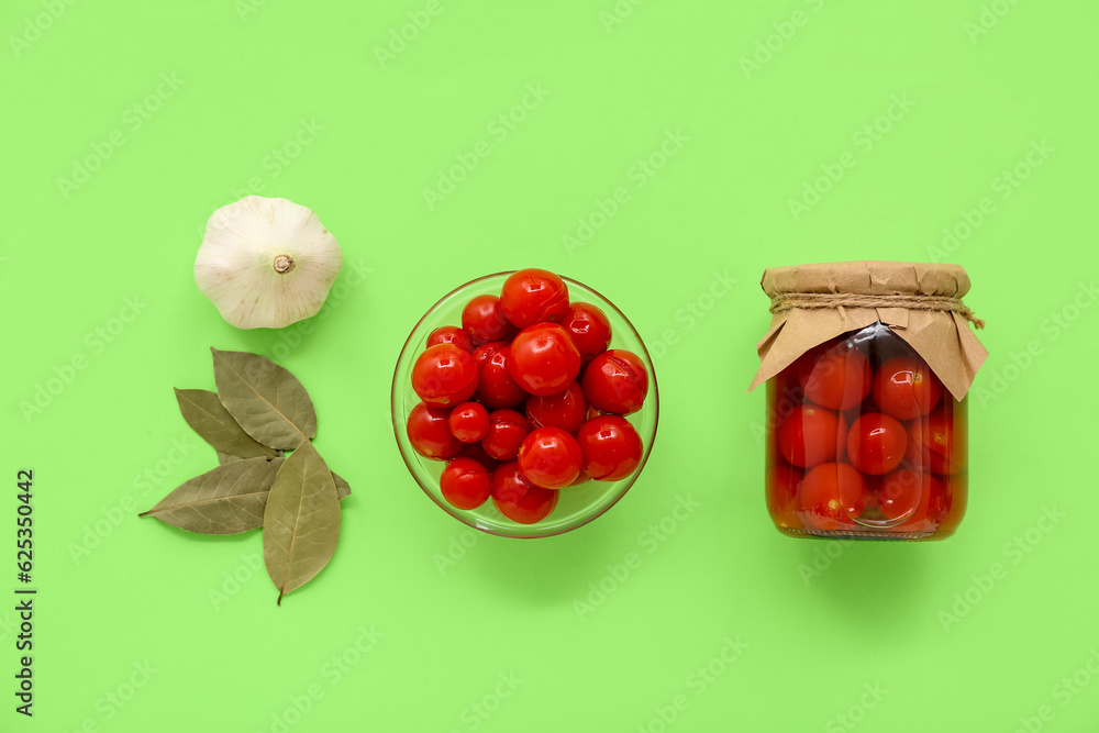 Jar and bowl with canned tomatoes on green background