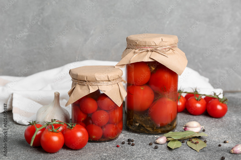 Jars with canned tomatoes and garlic on grey background