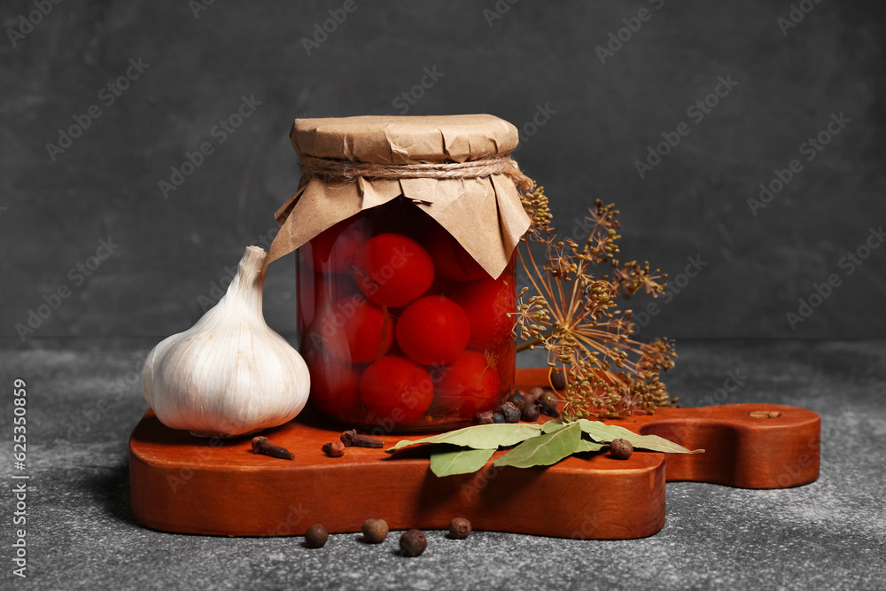 Jar with canned tomatoes and garlic on grey background