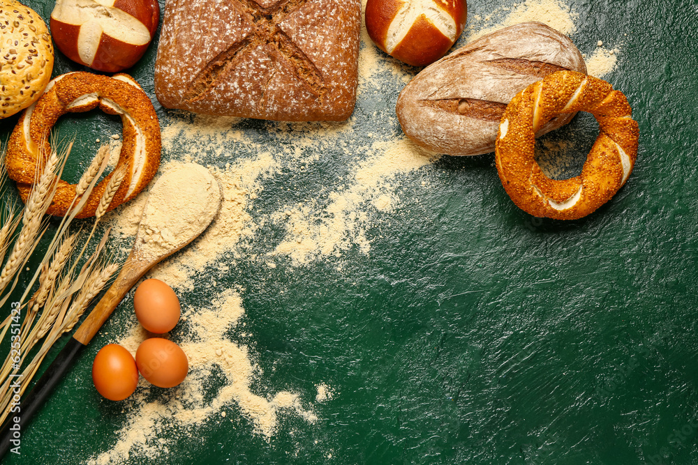 Different types of bread, flour, eggs and wheat ears on green table