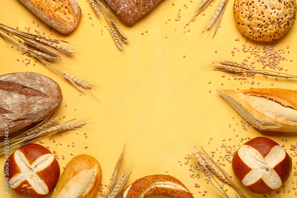 Frame made of different types of bread and wheat ears on yellow background