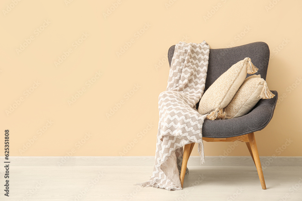 Grey armchair with cozy blanket and cushions near beige wall