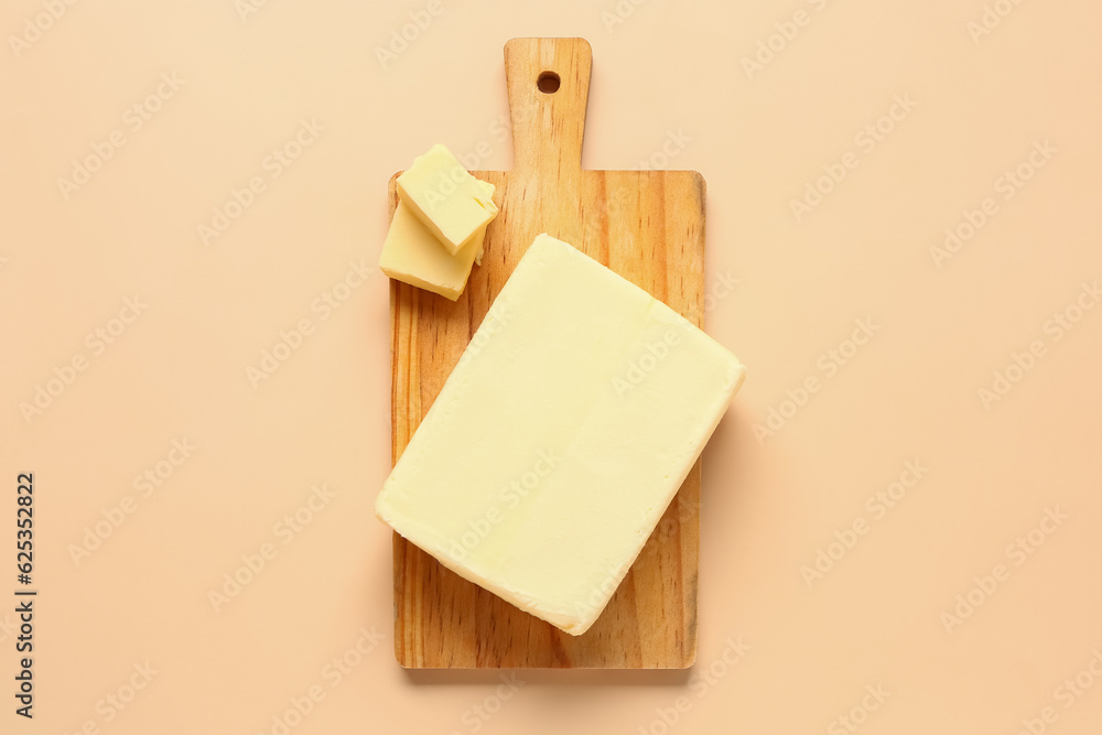 Wooden board with fresh butter on orange background