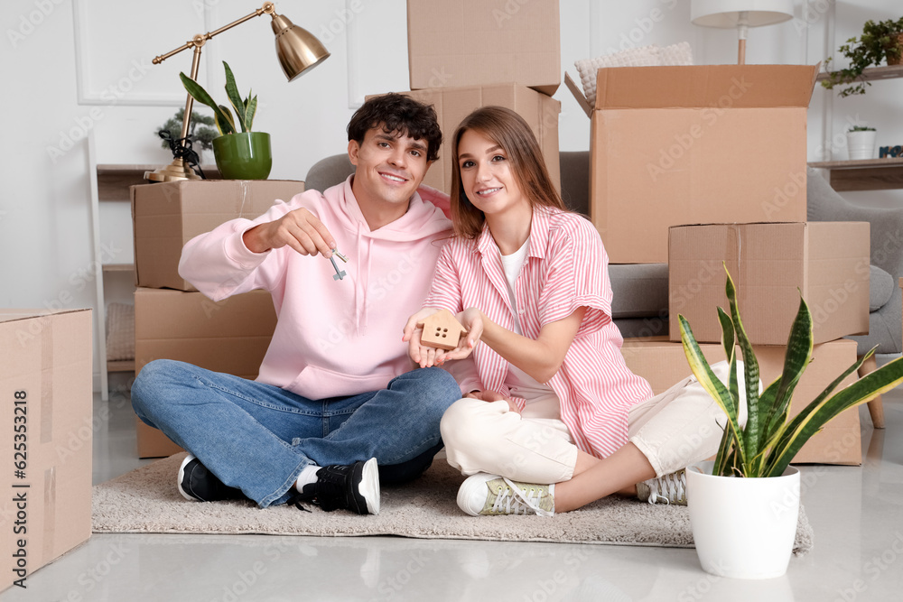 Young couple with keys and house figure in their new flat