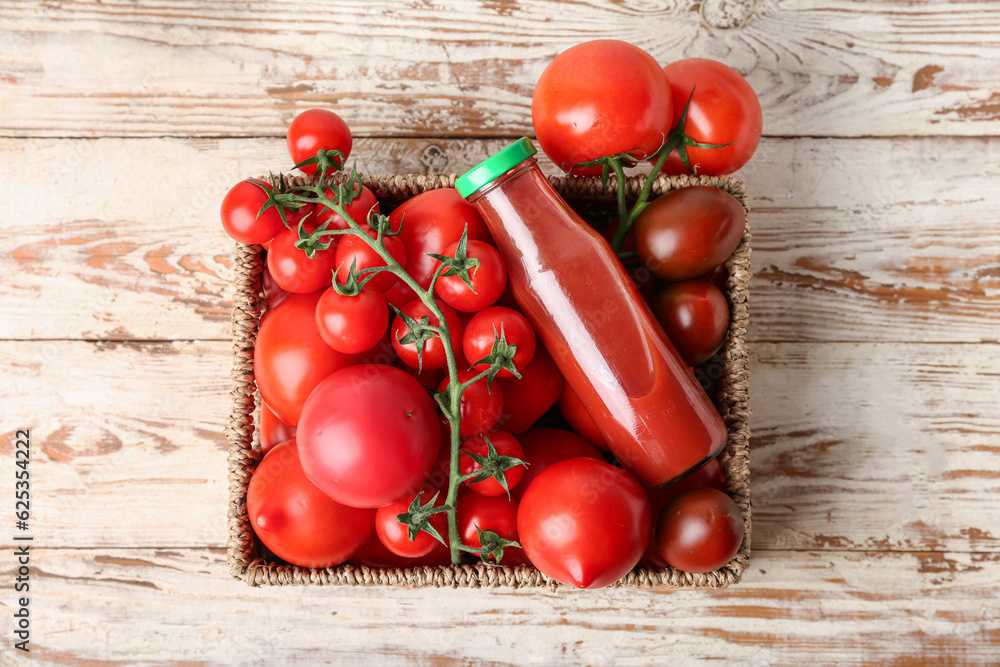 Wicker box with fresh tomatoes and bottle of juice on light wooden background