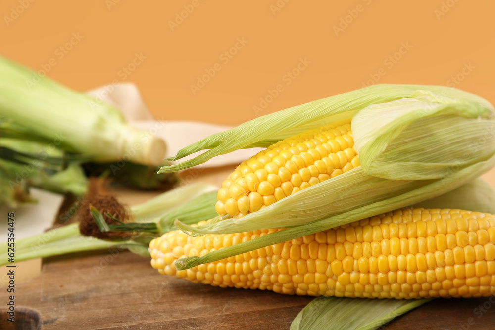 Wooden board with fresh corn cobs on brown background