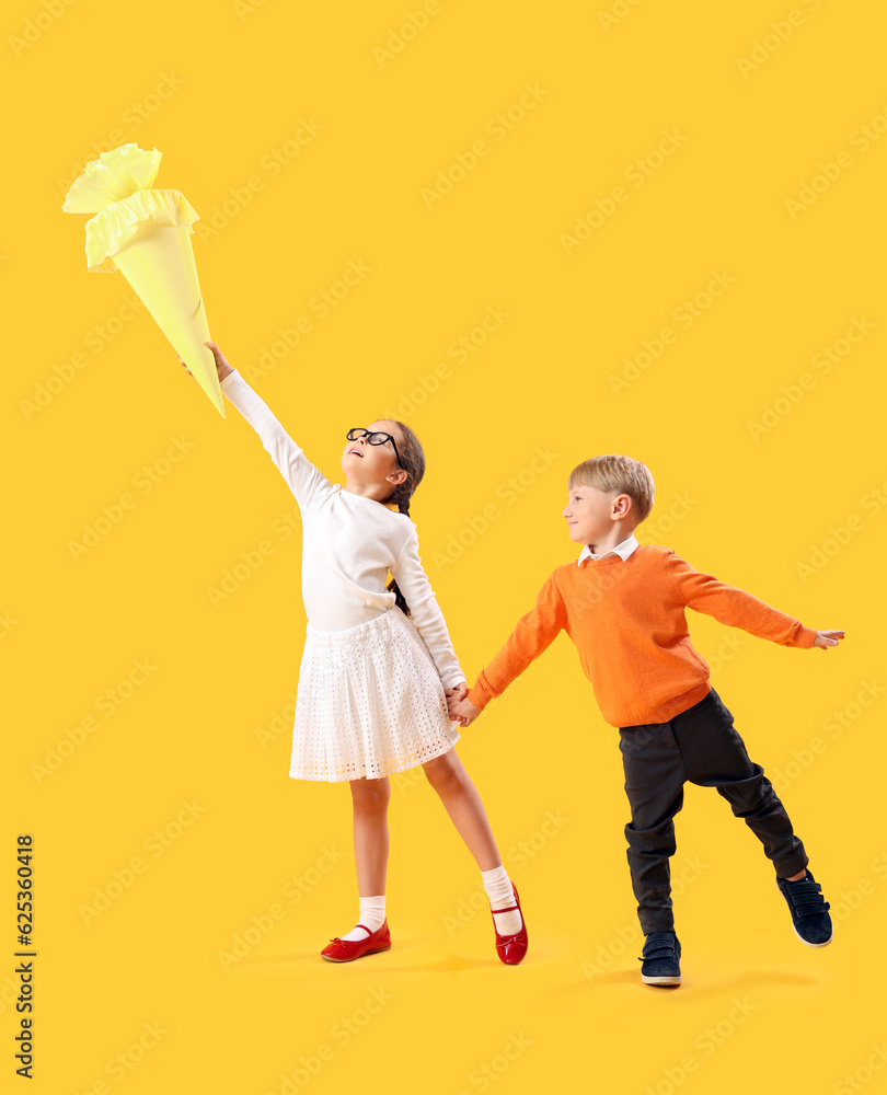 Happy little girl and boy with school cone jumping on yellow background