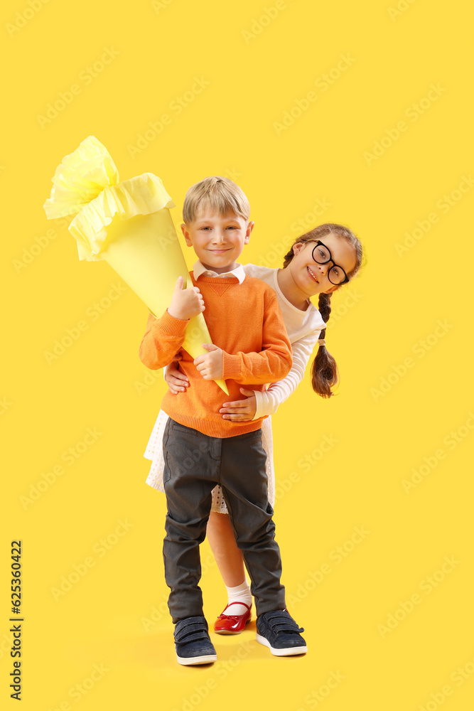 Happy little girl and boy with school cone on yellow background