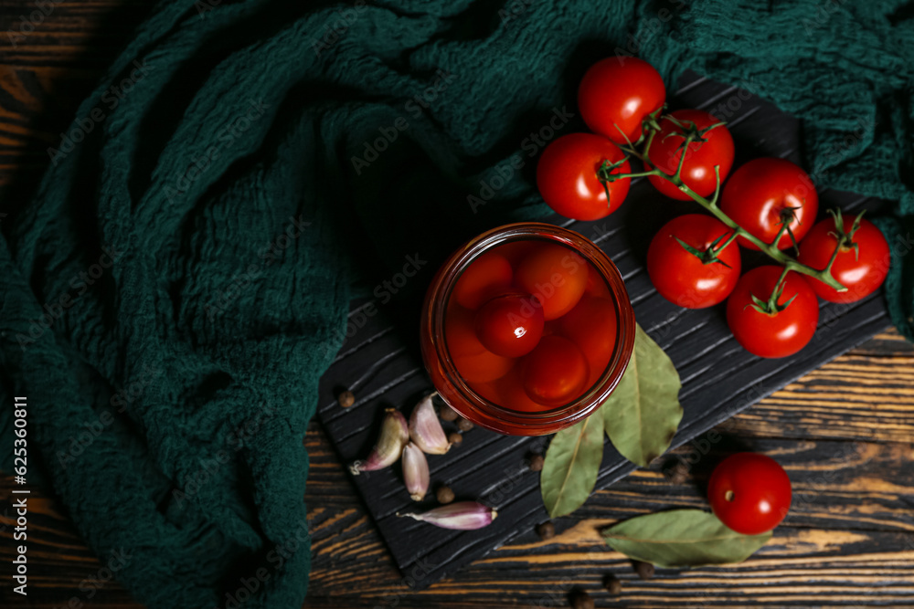 Jar with canned tomatoes and garlic on wooden background