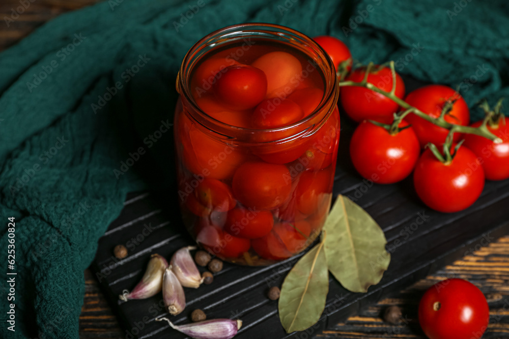 Jar with canned tomatoes and garlic on wooden background