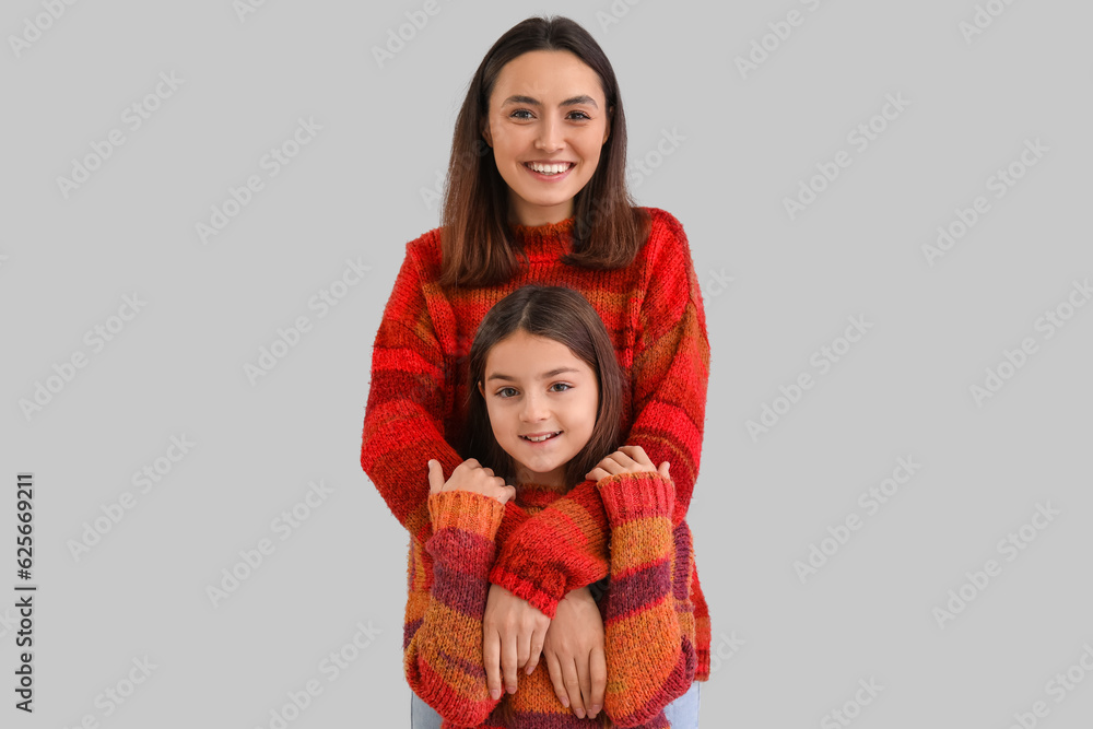 Little girl and her mother in warm sweaters hugging on grey background