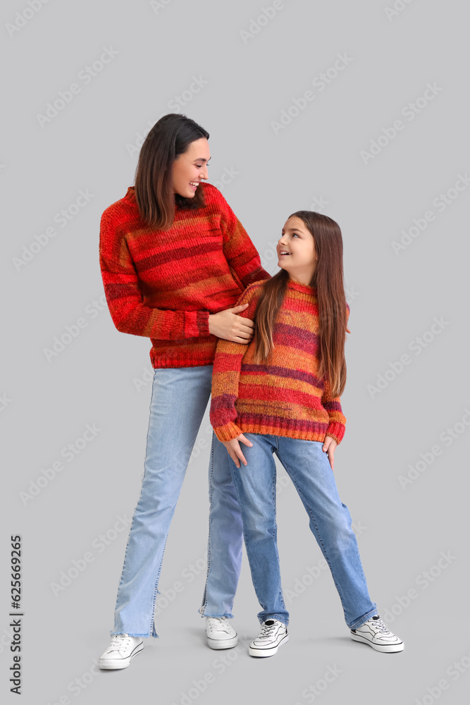 Little girl and her mother in warm sweaters on grey background