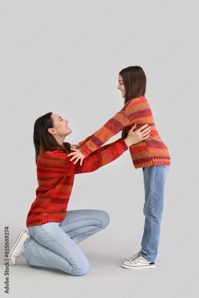 Little girl and her mother in warm sweaters on grey background