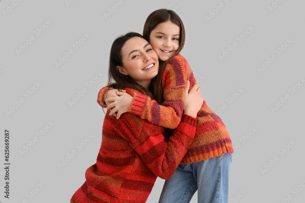 Little girl and her mother in warm sweaters hugging on grey background