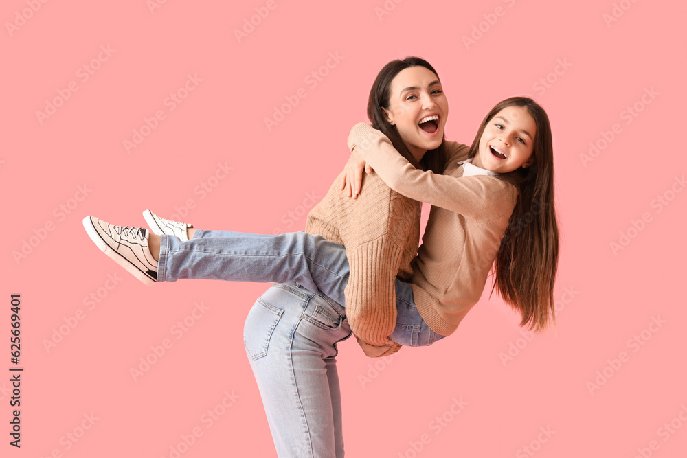 Happy little girl and her mother in knitted sweaters on pink background