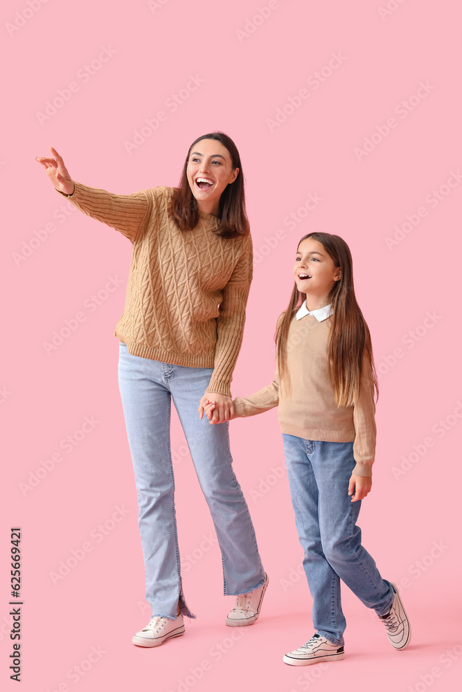 Little girl and her mother in knitted sweaters holding hands on pink background