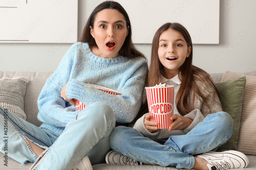 Little girl and her mother in warm sweaters with popcorn watching TV at home