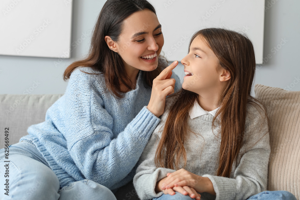 Happy mother touching her little daughters nose at home