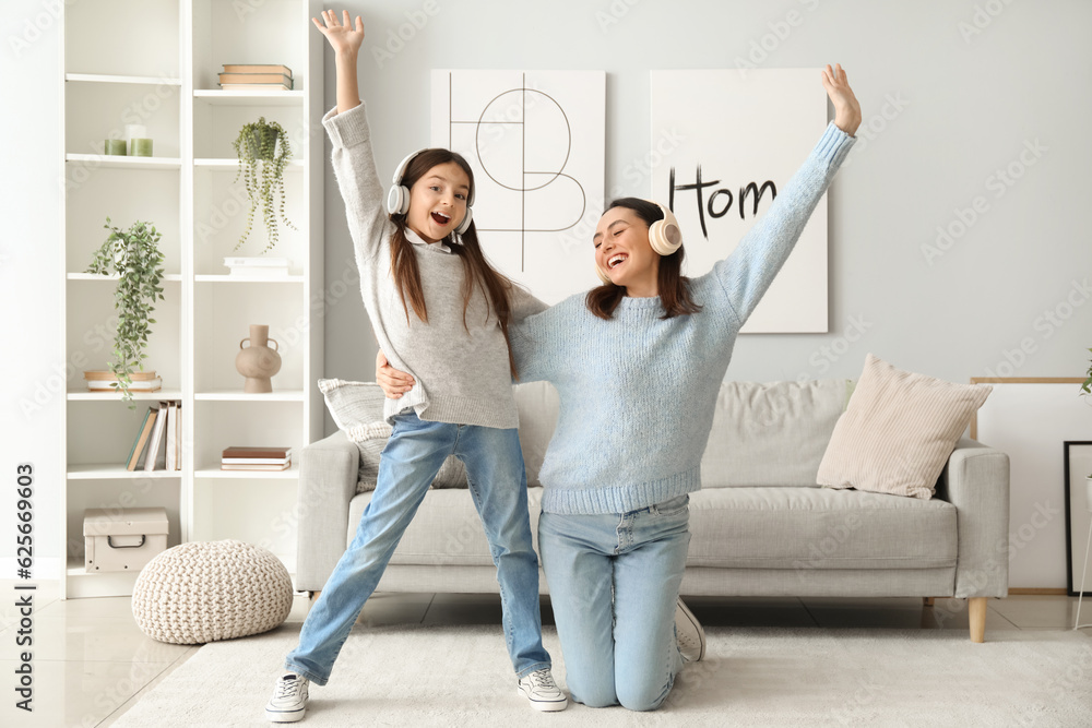 Little girl and her mother in sweaters and headphones dancing at home