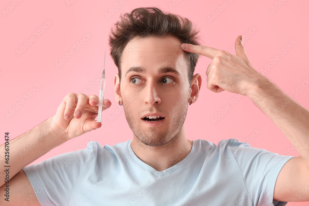 Young man with injection for hair growth on pink background, closeup