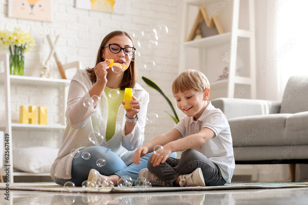 Nanny with little boy blowing soap bubbles at home