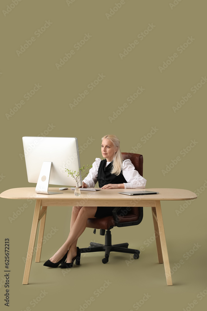 Mature female programmer working with computer at table on green background