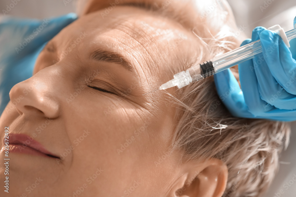 Mature woman receiving filler injection in beauty salon, closeup