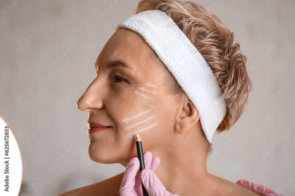 Beautician marking mature womans face for filler injection in salon, closeup