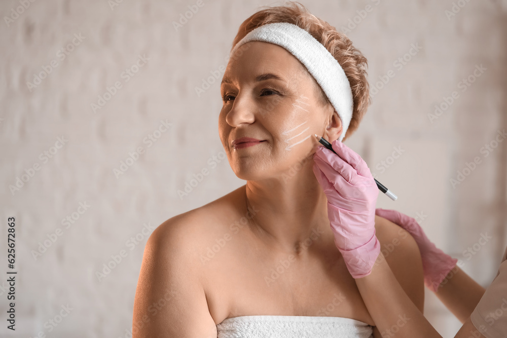 Beautician marking mature womans face for filler injection in salon, closeup