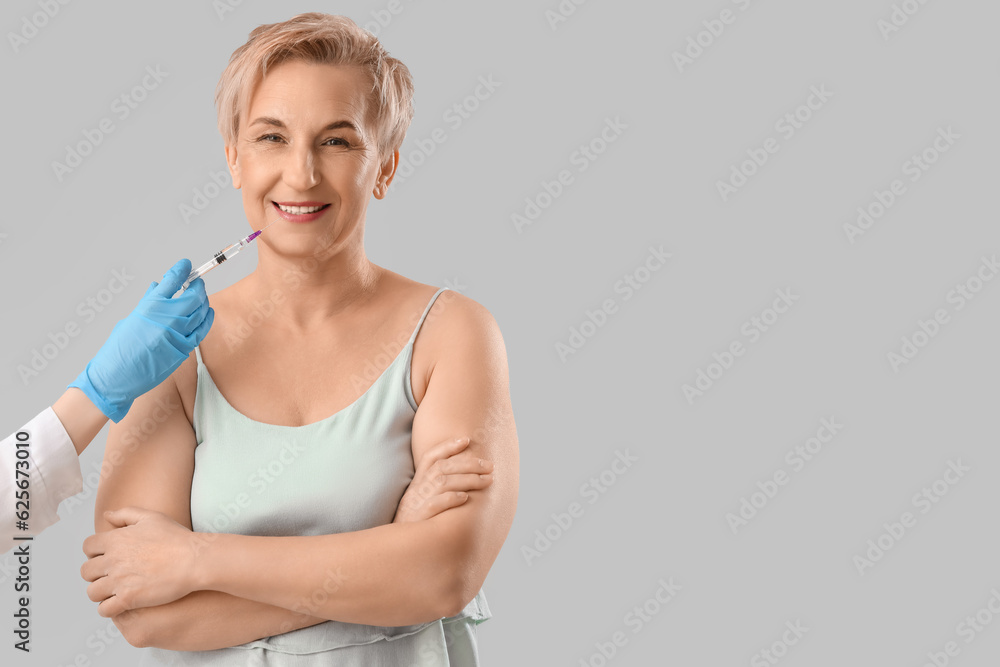 Mature woman receiving filler injection on light background