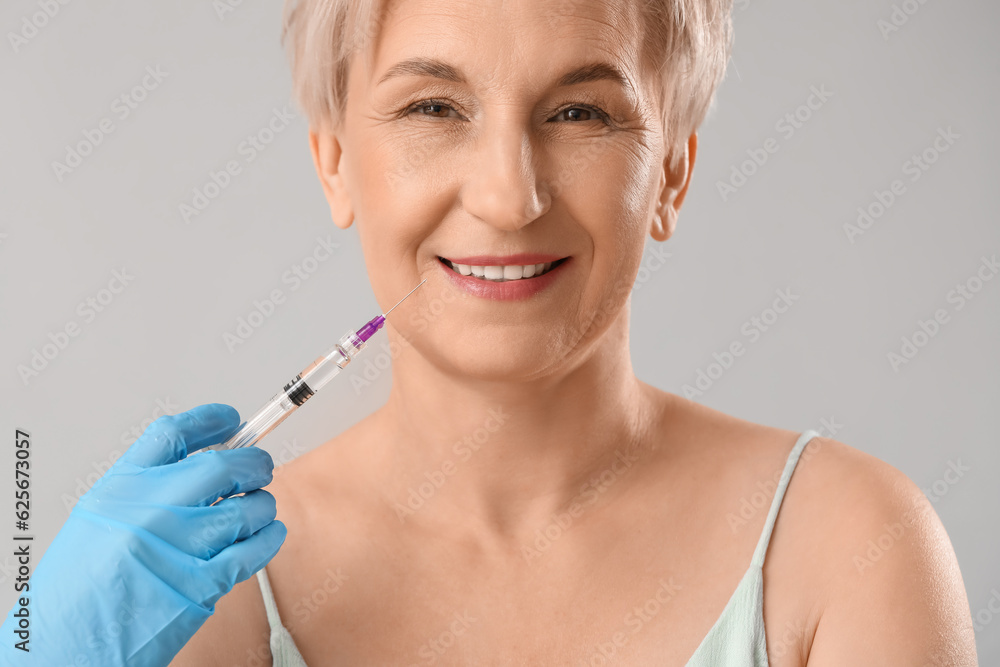 Mature woman receiving filler injection on light background