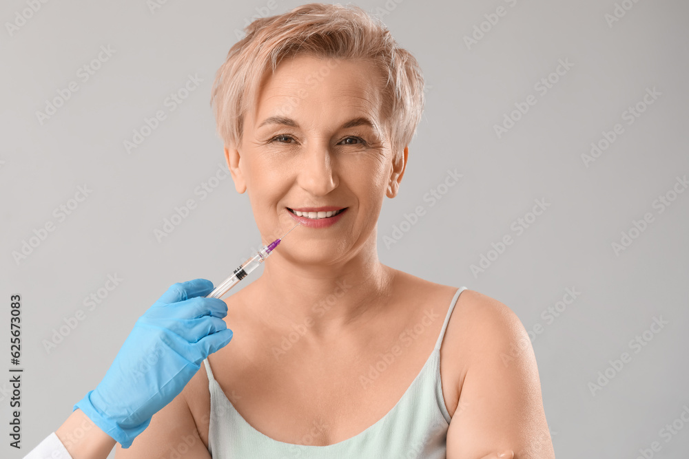 Mature woman receiving filler injection on light background