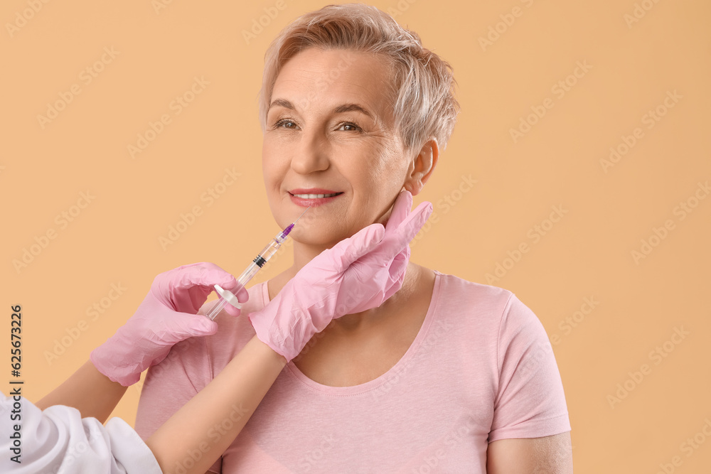 Mature woman receiving lip filler injection on beige background