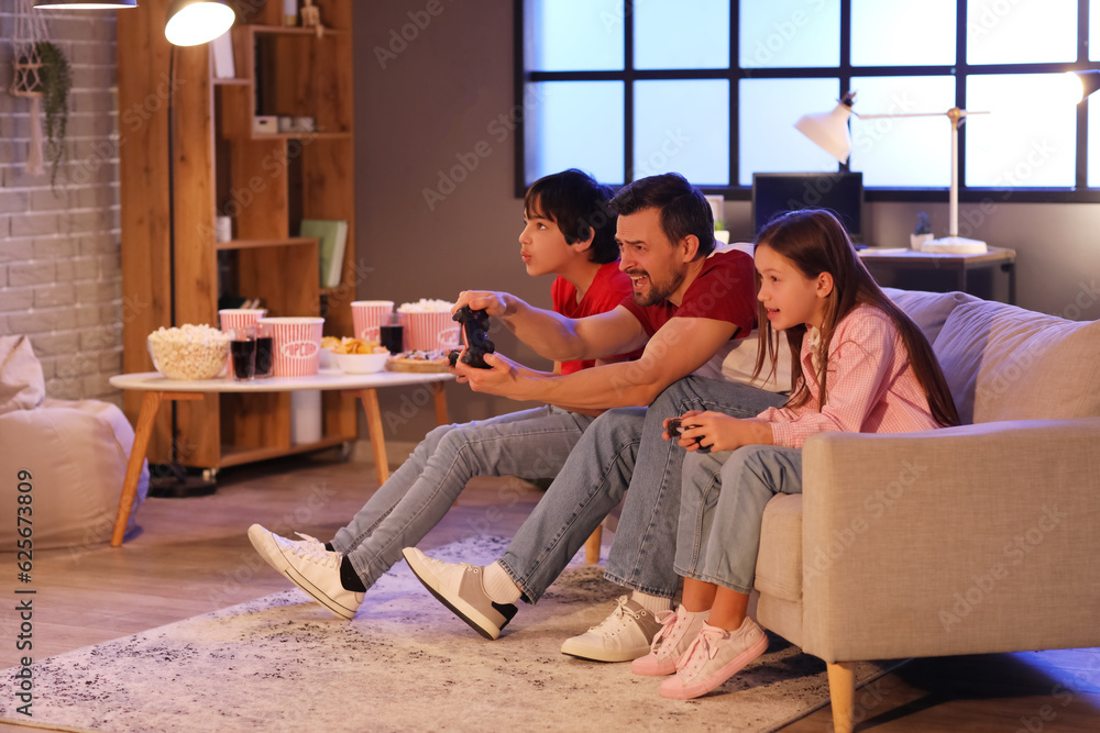 Father with his little children playing video game at home in evening