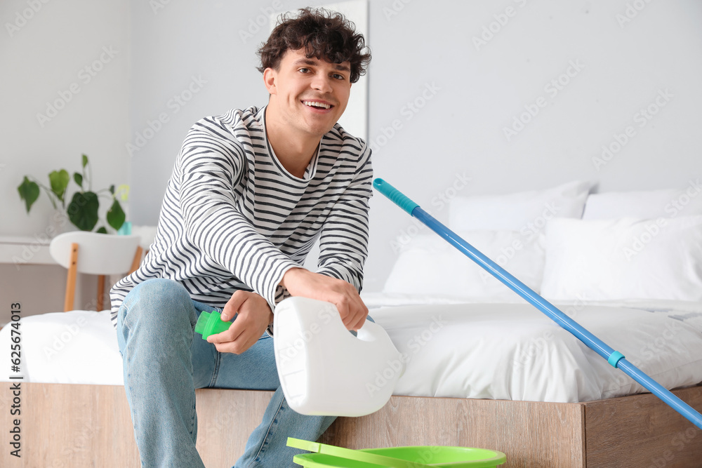 Young man pouring detergent into bucket in bedroom