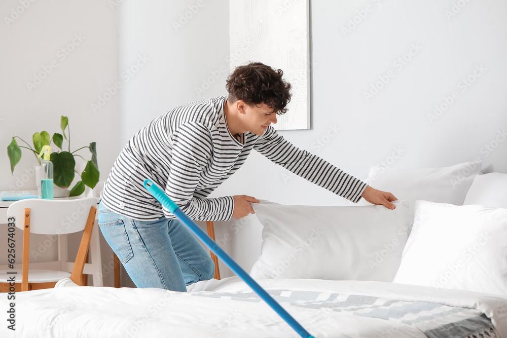 Young man making his bed at home