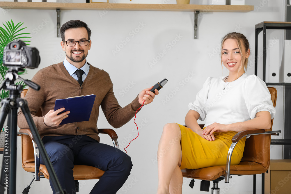 Male journalist with microphone having an interview with woman in studio