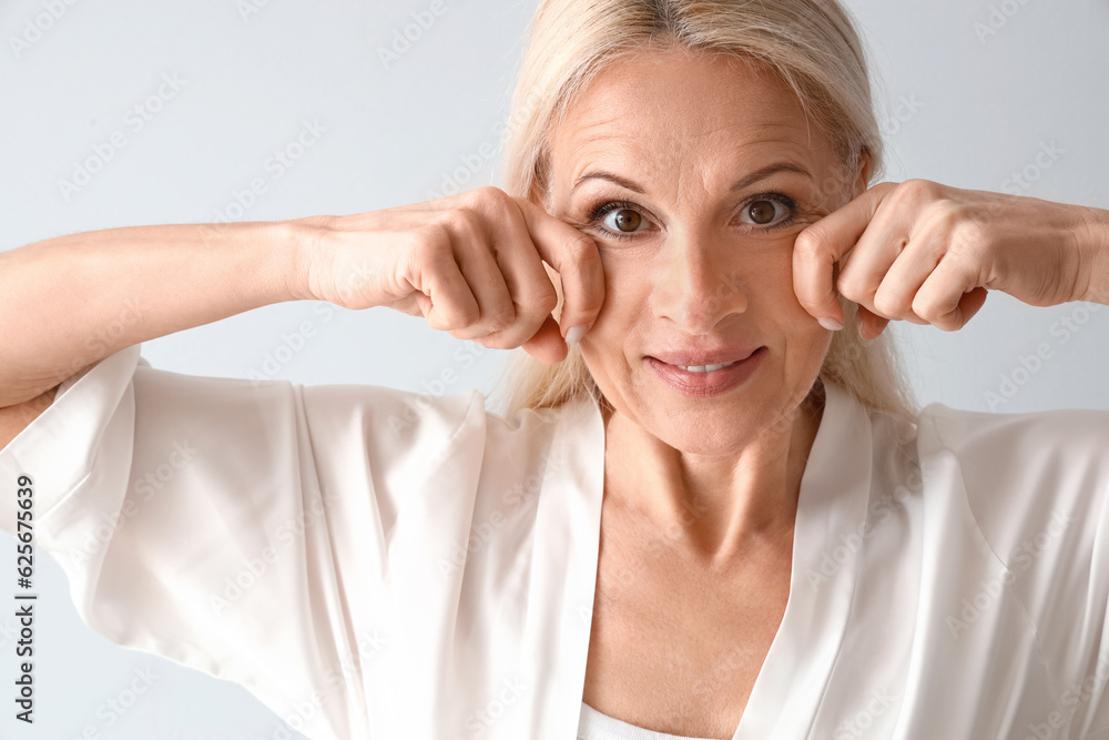 Mature woman doing face building exercise on light background, closeup