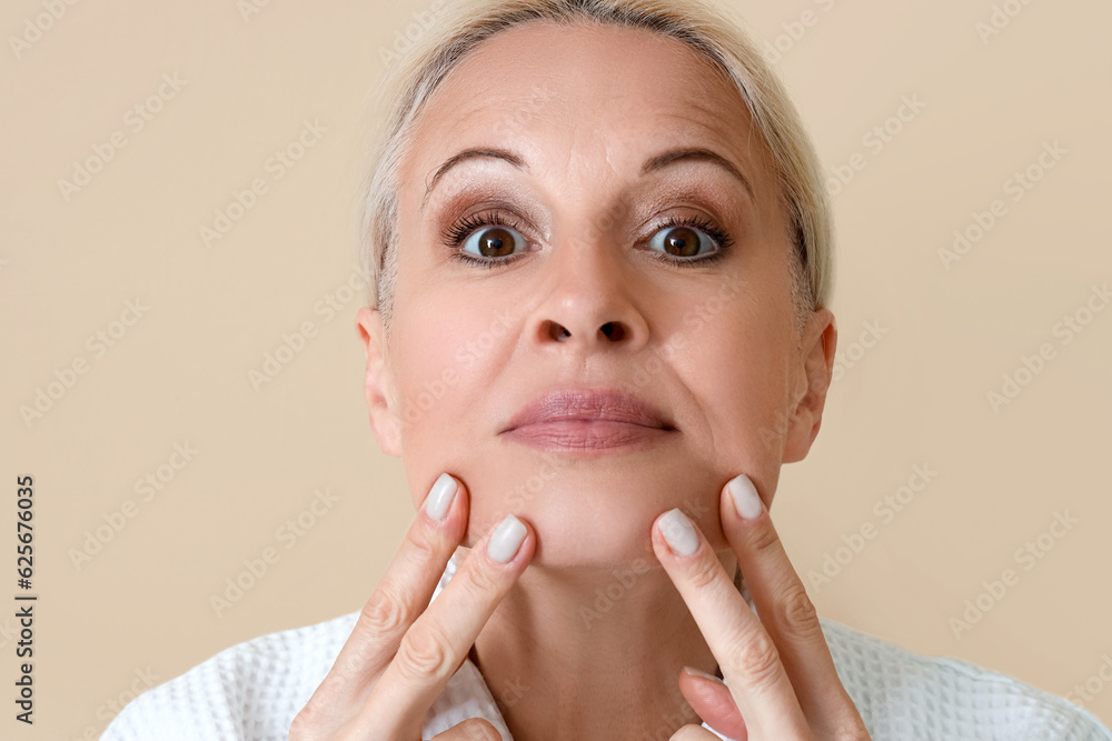 Mature woman doing face building exercise on beige background, closeup