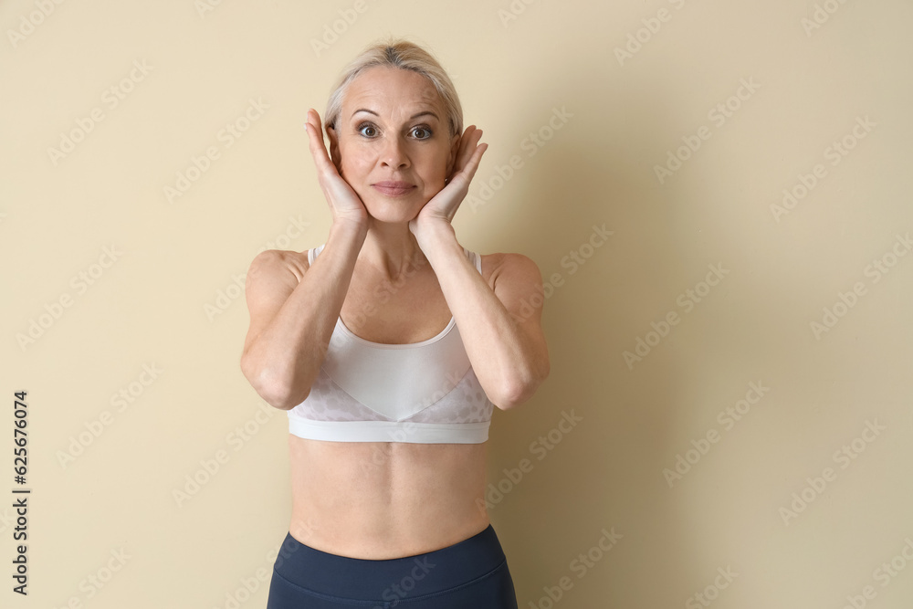 Sporty mature woman doing face building exercise on beige background