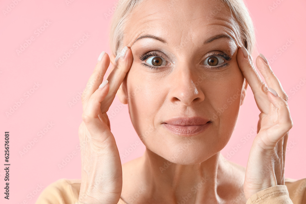 Mature woman doing face building exercise on pink background, closeup