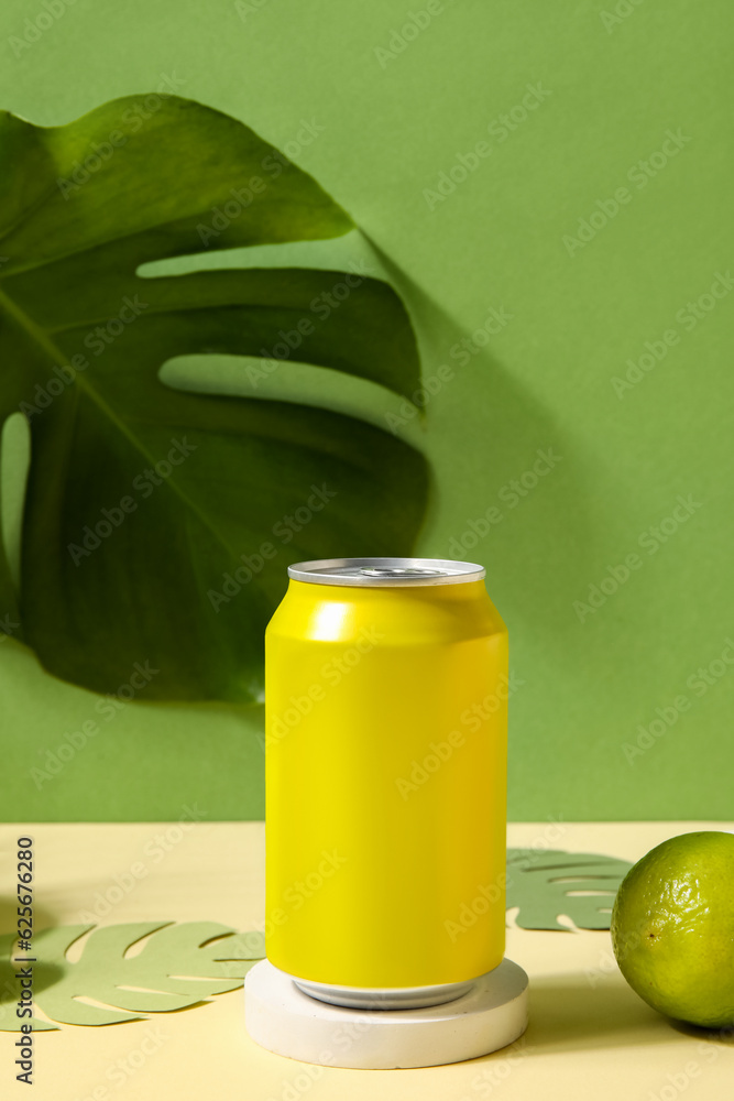 Podium with can of soda, lime and paper palm leaves on table near green wall