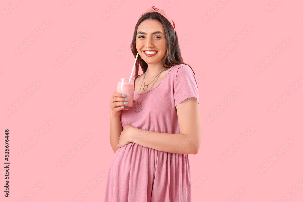 Young pregnant woman with glass of smoothie on pink background