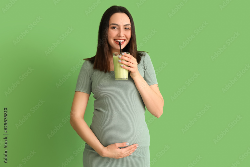 Young pregnant woman drinking smoothie on green background